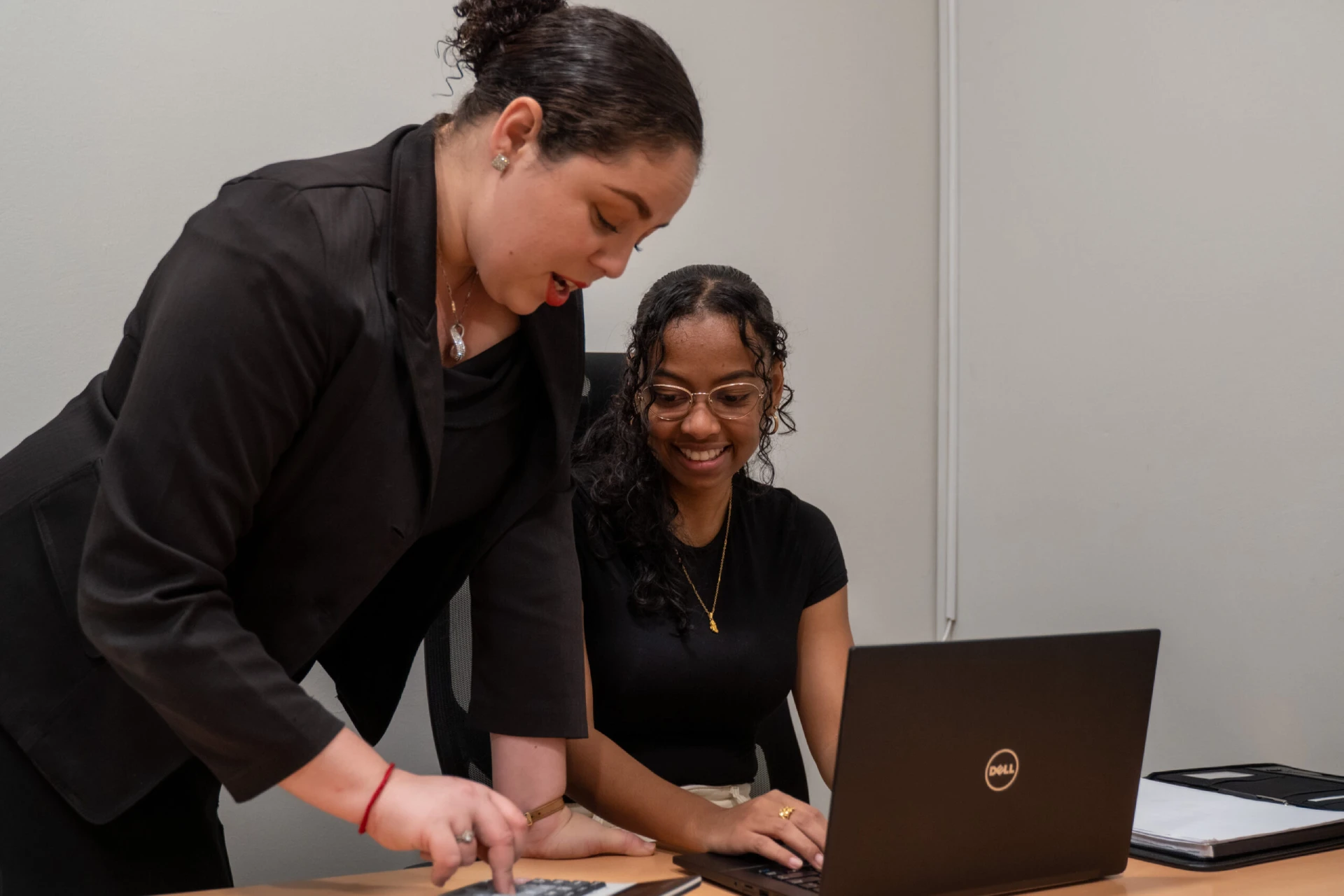 Two businesswomen watching a presentation on a wall-mounted screen in a meeting room.